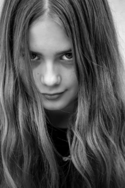 schwarzweiss-Foto eines langhaarigen Mädchens mit großen, brauen Augen, das in die Camera blickt